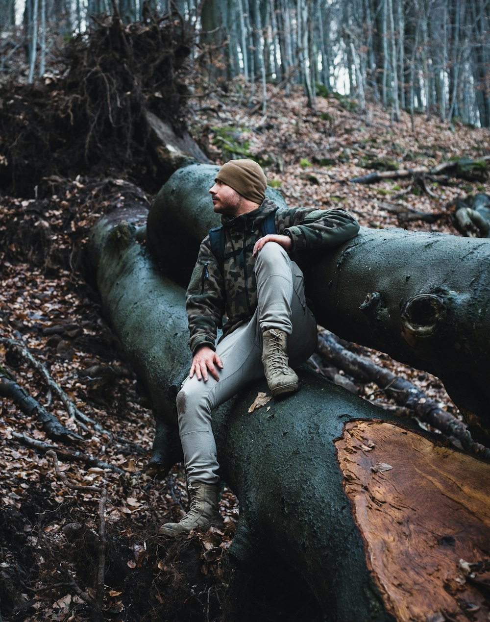 man in black jacket and brown pants lying on tree trunk