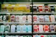 Shelves display a variety of smartphone cases in multiple colors, arranged in an organized manner within a store. A sign in Cyrillic characters and advertisements for mobile network plans are visible above the cases.