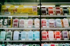 Shelves display a variety of smartphone cases in multiple colors, arranged in an organized manner within a store. A sign in Cyrillic characters and advertisements for mobile network plans are visible above the cases.