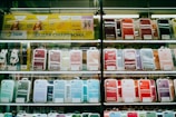 Shelves display a variety of smartphone cases in multiple colors, arranged in an organized manner within a store. A sign in Cyrillic characters and advertisements for mobile network plans are visible above the cases.