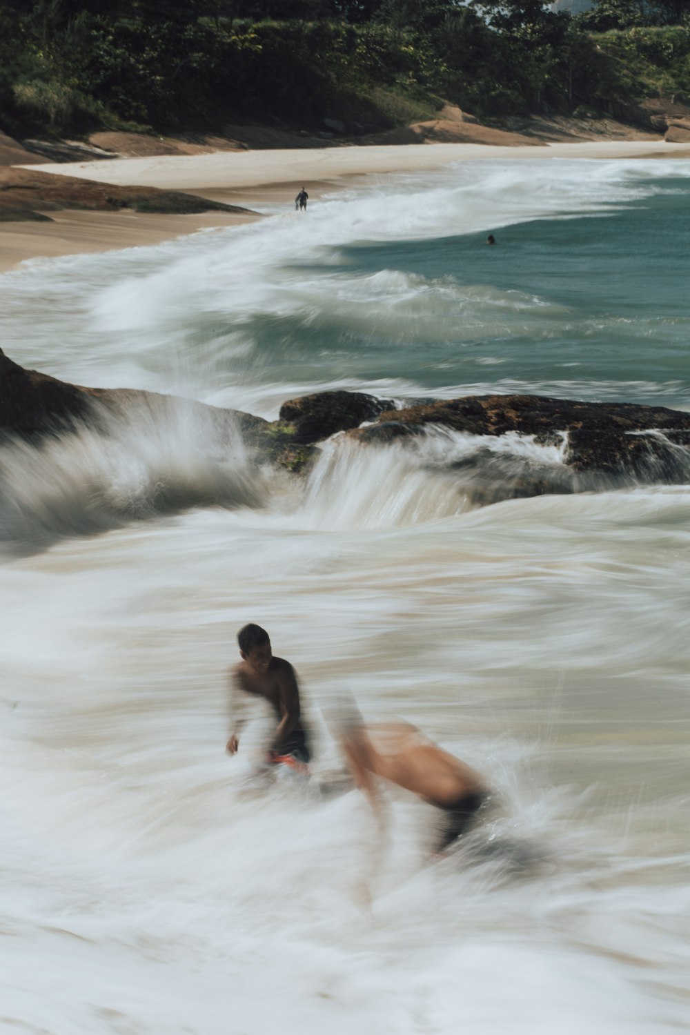 homem de shorts pretos sentado na rocha marrom perto das ondas do oceano durante o dia