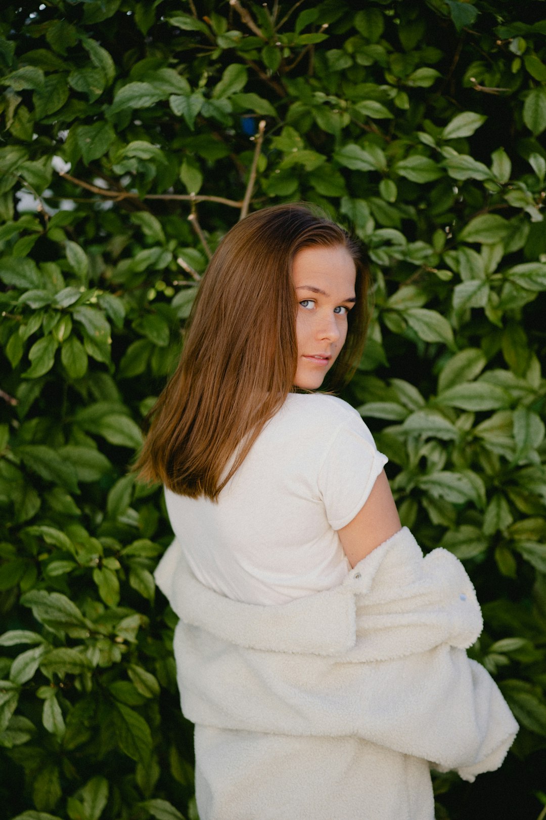 woman in white long sleeve shirt standing near green plant