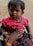 A young child with short, dark hair and a small decorative mark on their forehead is wearing a bright pink top with black lettering and dark jeans. They are held gently by an adult's hand adorned with rings and bracelets, complementing the child’s bracelets. The background is neutral and unobtrusive.