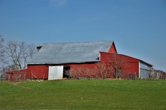 A barndominium with a metal roof and wraparound porch surrounded by open fields.