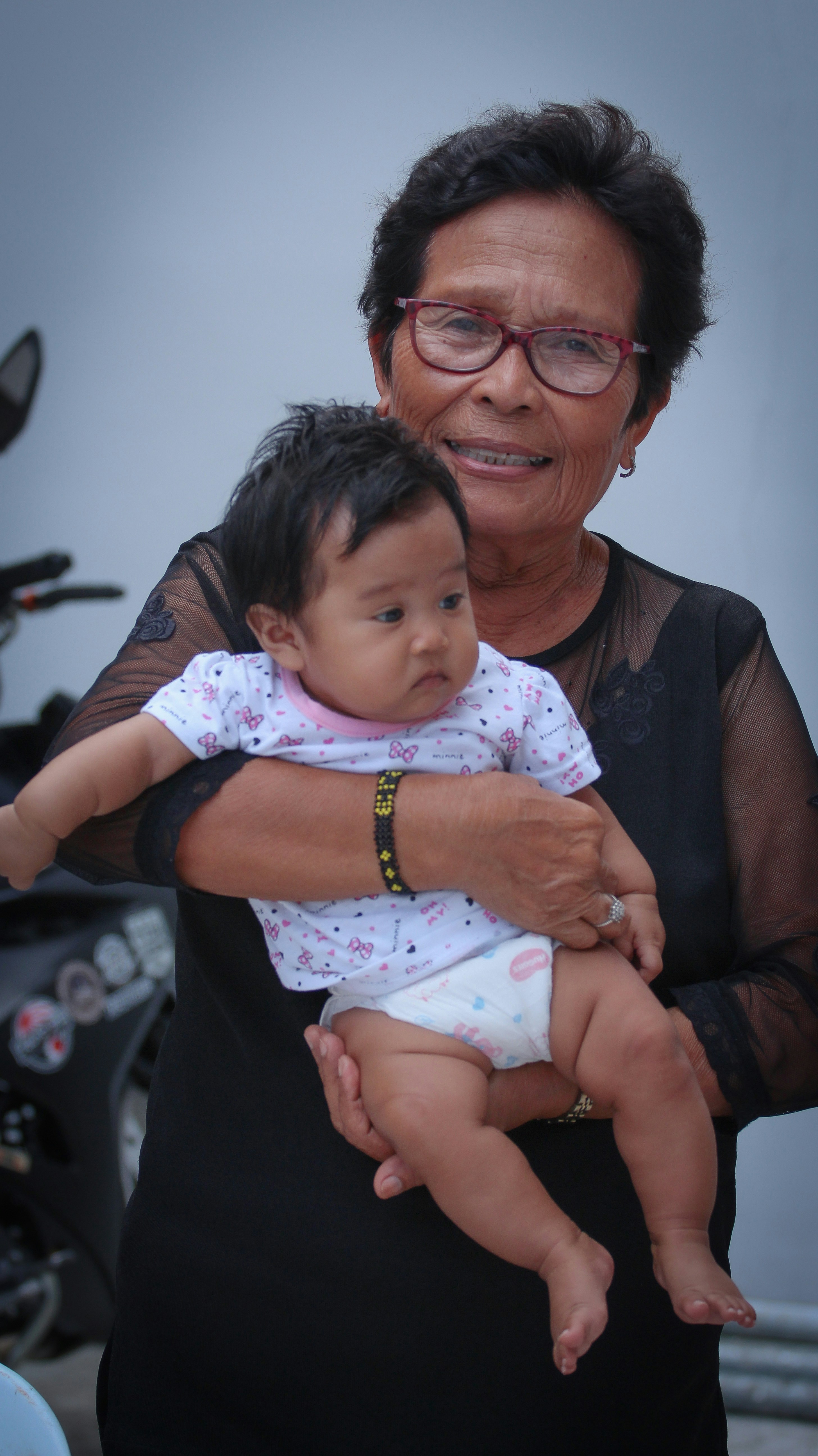 wanita dengan kardigan hitam menggendong bayi dengan onesie putih