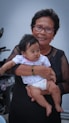 woman in black cardigan carrying baby in white onesie