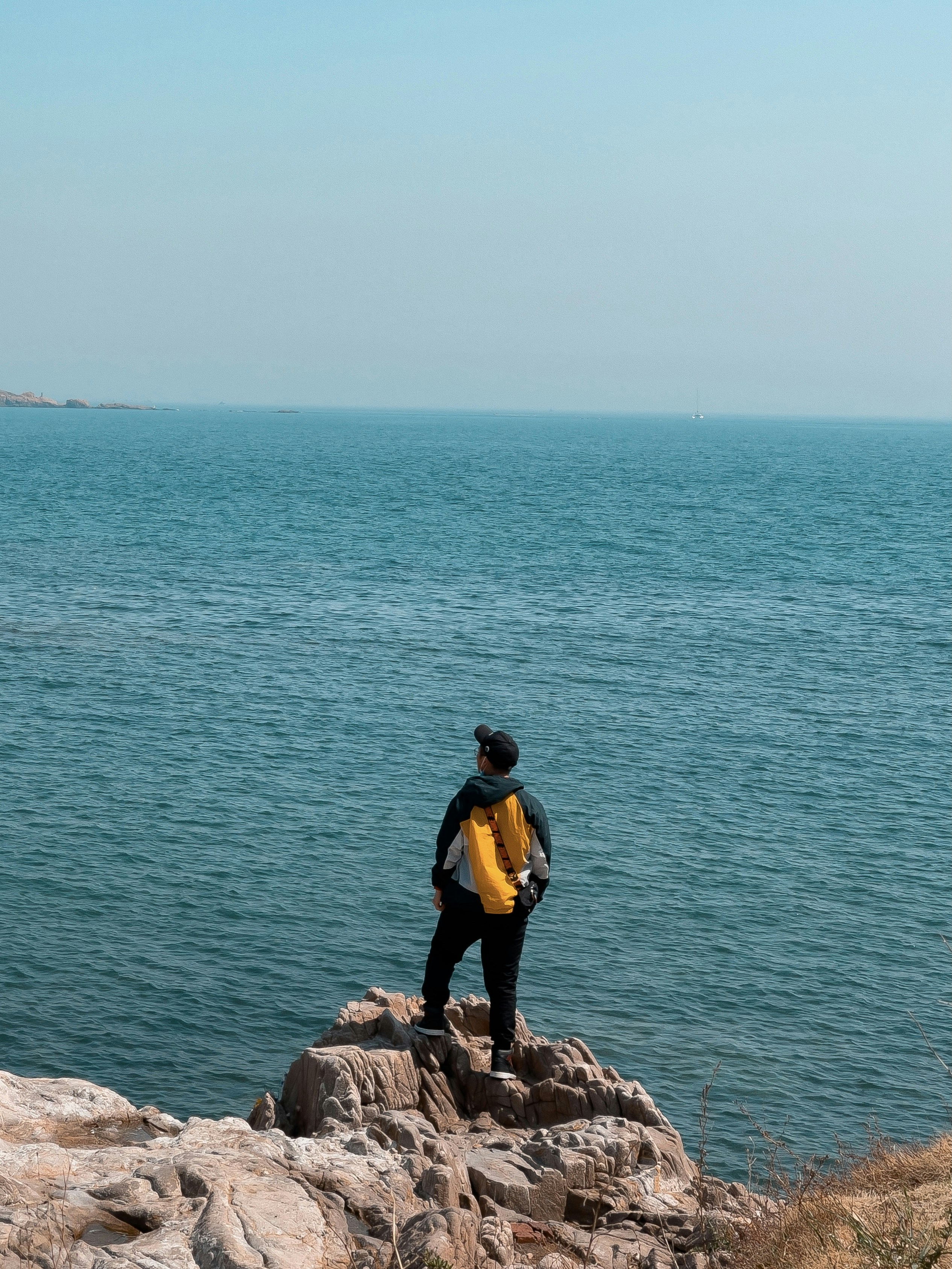 Man in yellow jacket and black pants standing on rock formation near ...