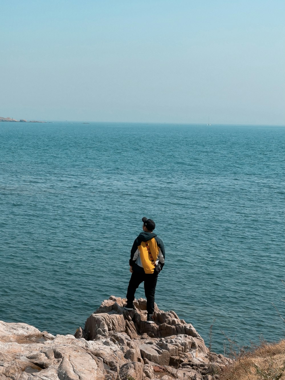 Homme en veste jaune et pantalon noir debout sur une formation rocheuse près du plan d’eau pendant