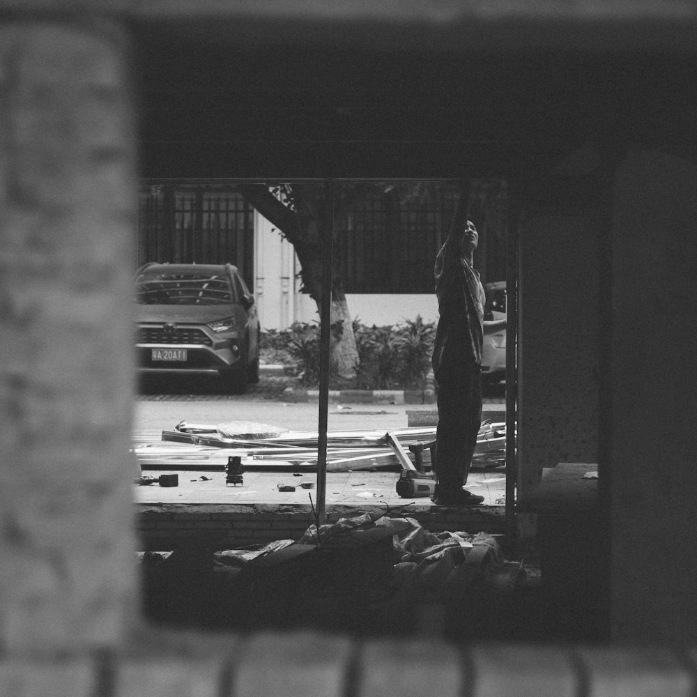 grayscale photo of man in black jacket and pants standing on wooden plank