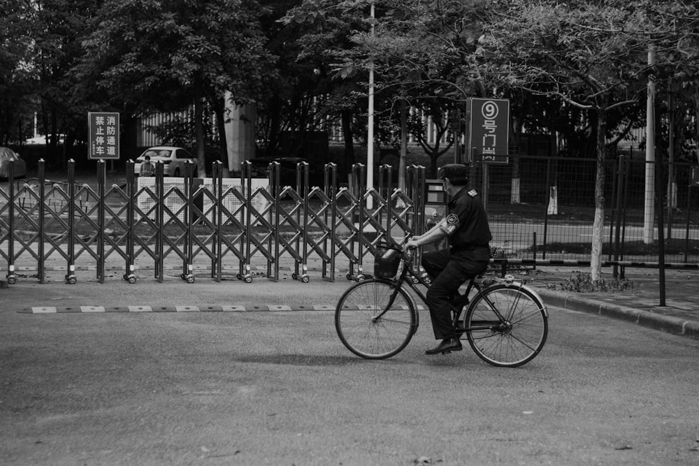 grayscale photo of man riding bicycle on road