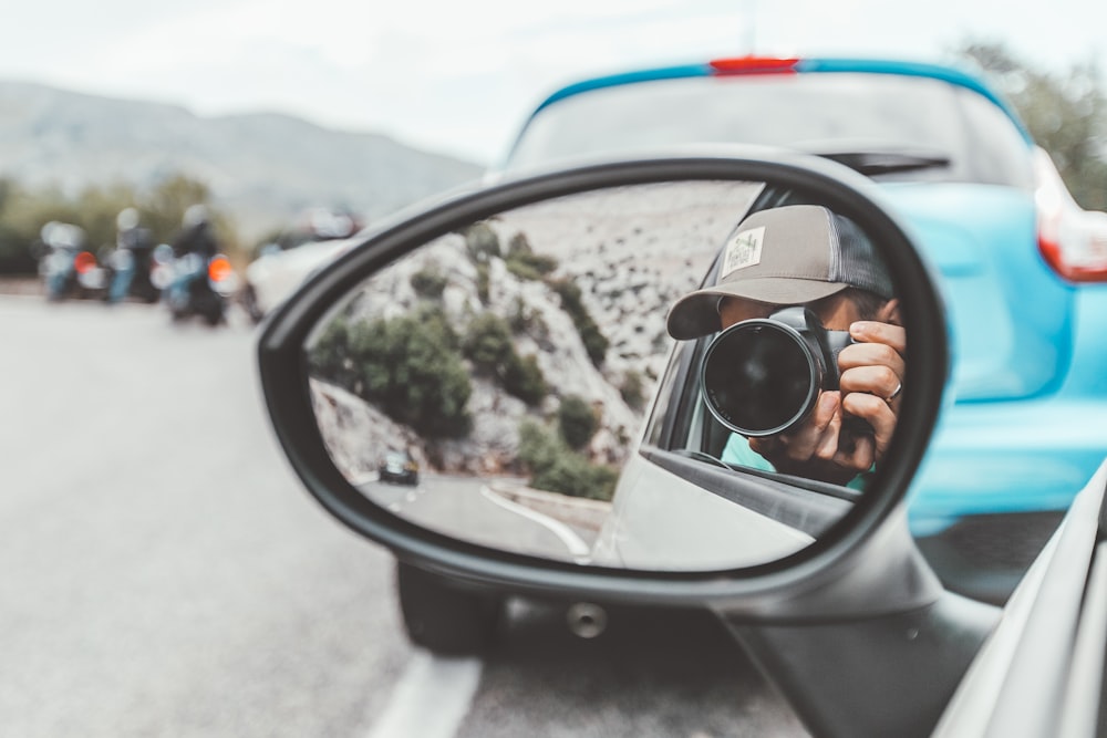 person taking photo of car side mirror