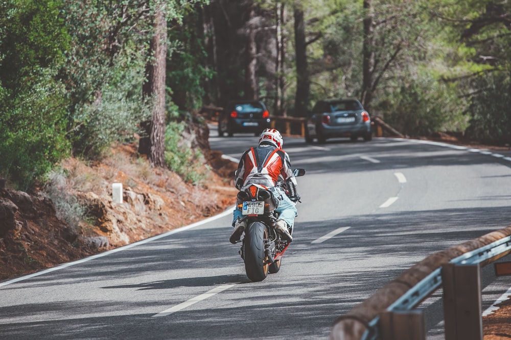 hombre en traje de motocicleta rojo y blanco montando motocicleta en la carretera durante el día