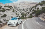A winding mountain road with a rental car parked beside a scenic overlook.