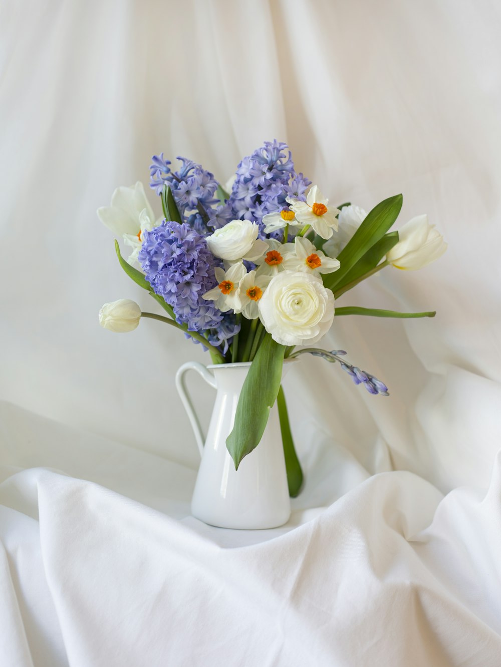 Ramo de flores blancas y moradas en jarrón de cerámica blanca