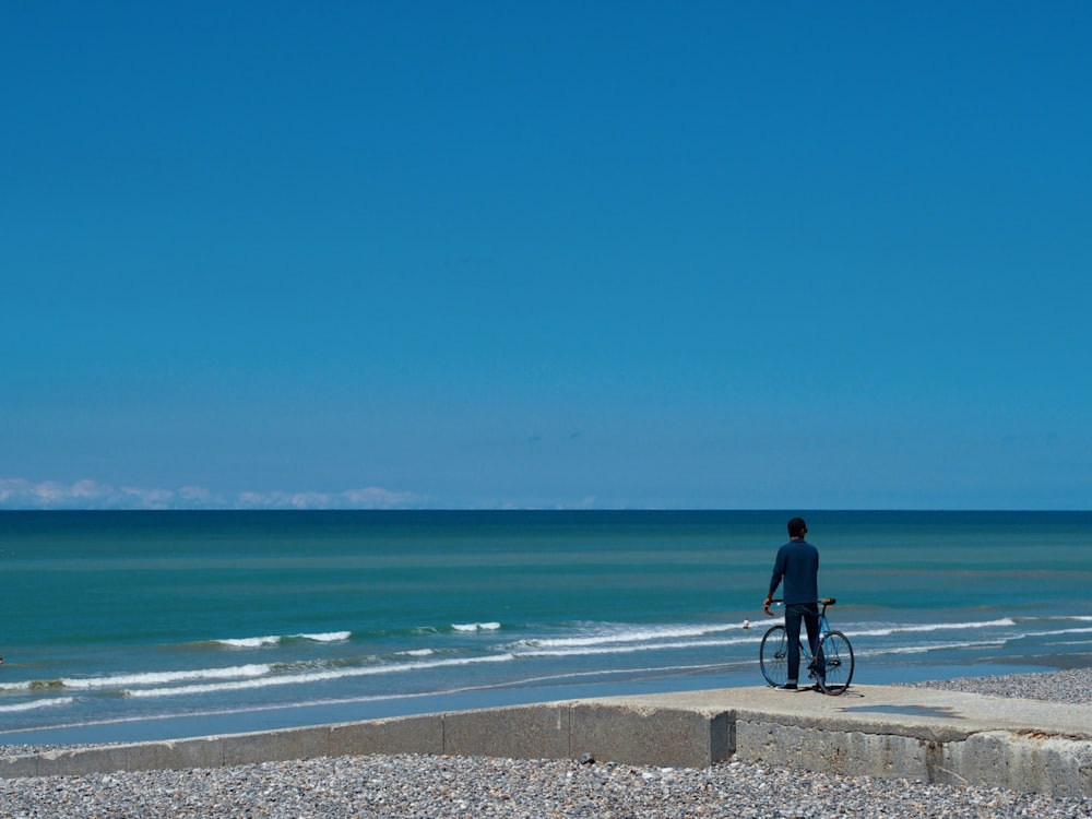 man in black jacket riding bicycle on beach during daytime