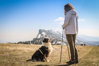 woman in white coat standing beside black and white dog on green grass field during daytime