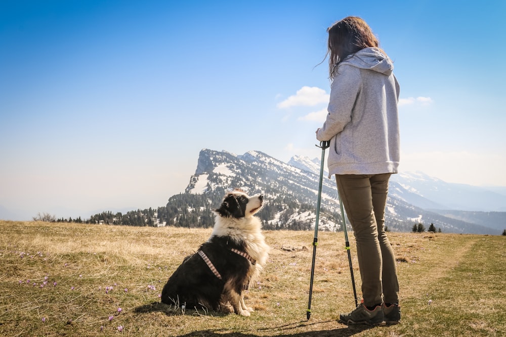 woman in white coat standing beside black and white dog on green grass field during daytime