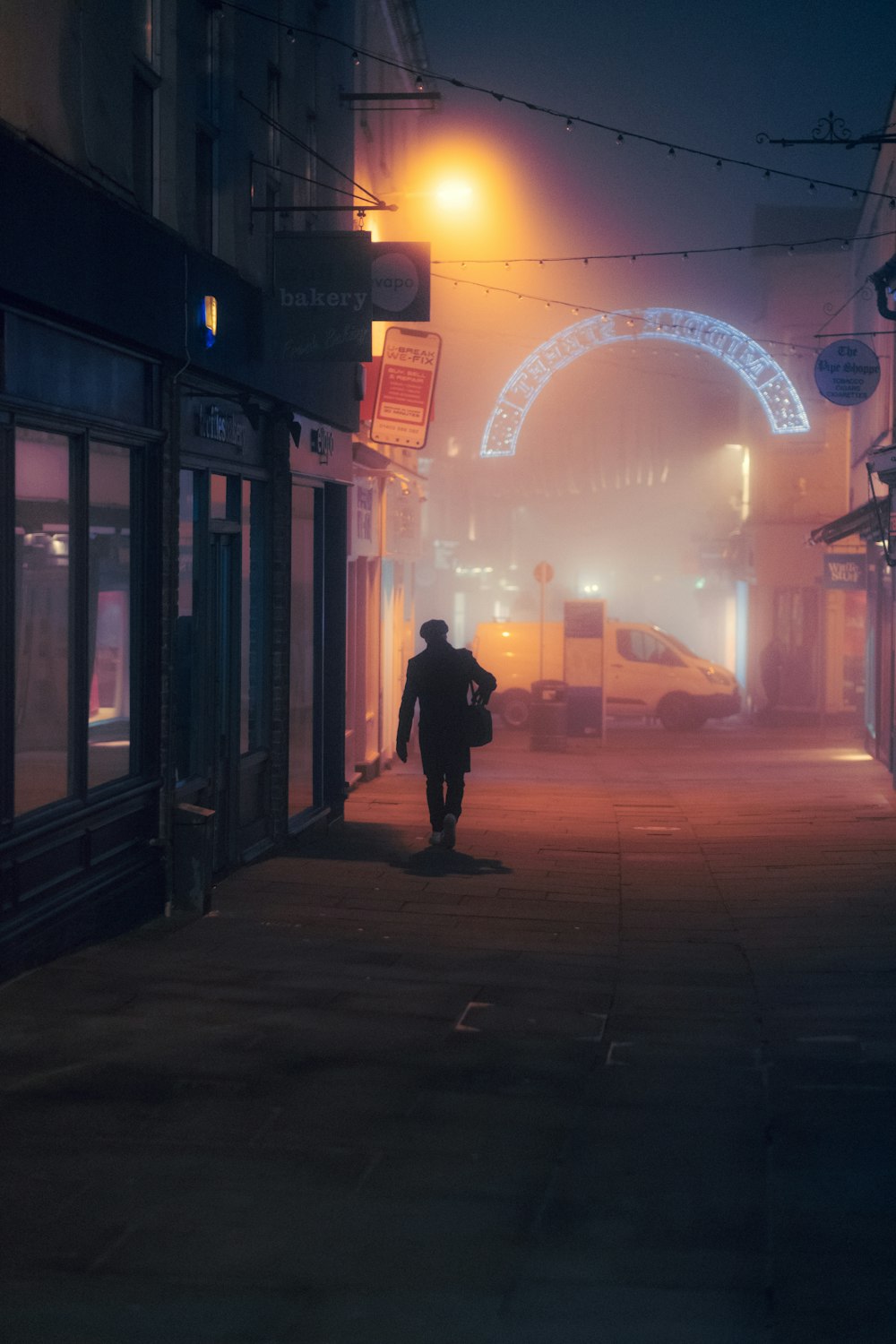 homme en veste noire marchant sur le trottoir pendant la nuit
