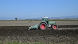 green tractor on brown field under blue sky during daytime