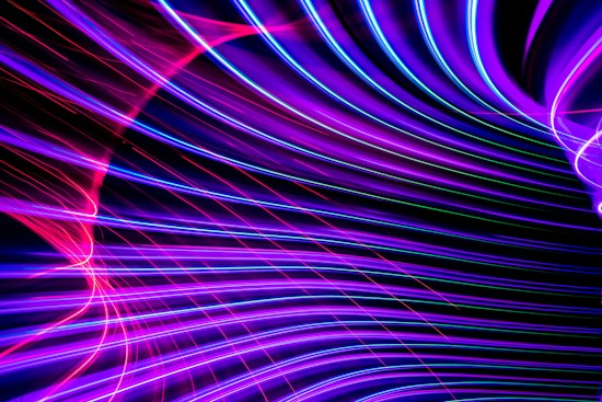 Vibrant neon lines in shades of purple, pink, and blue curve and intertwine against a dark background, creating a dynamic and abstract visual. The lines have a glowing effect, suggesting movement and energy.