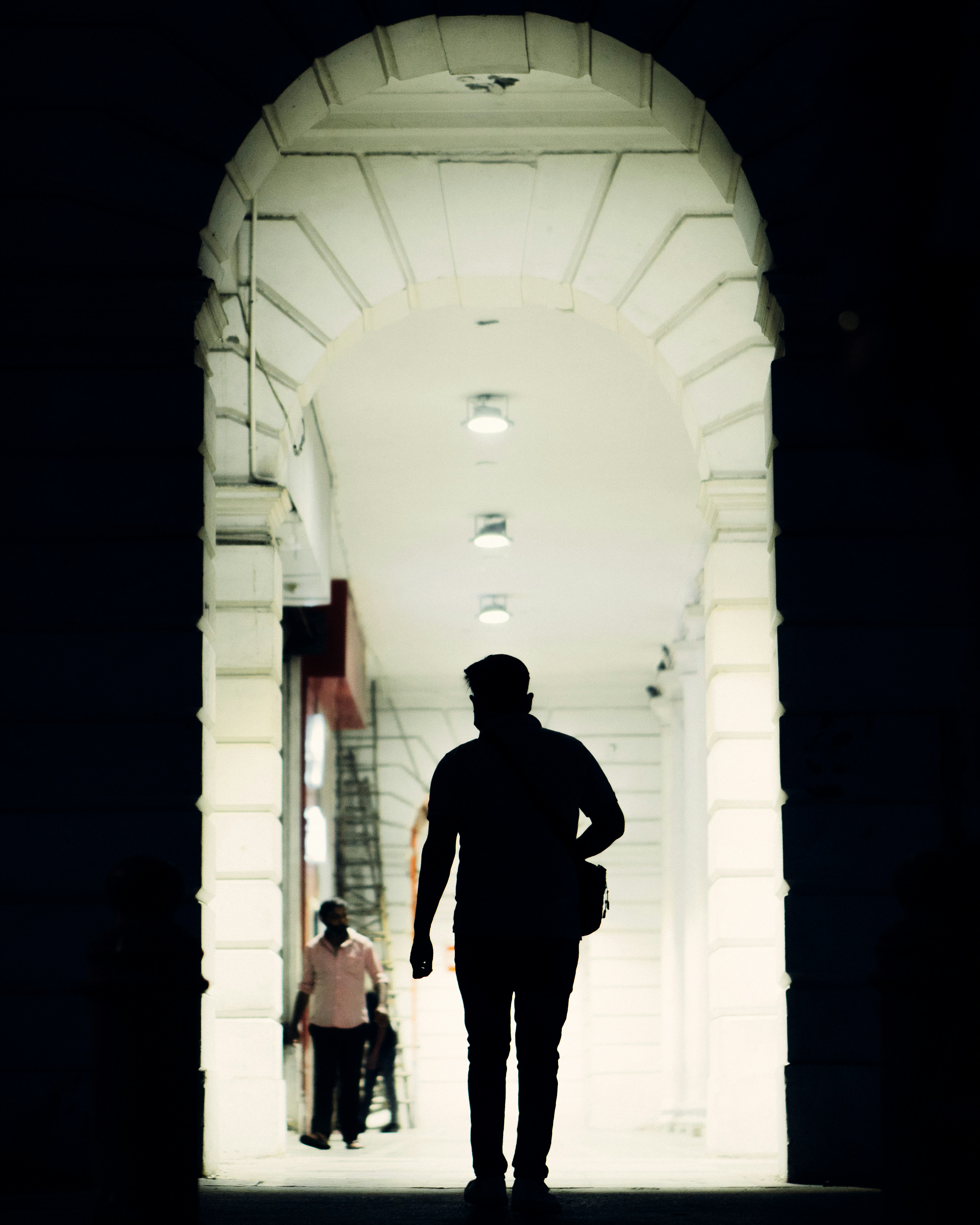 man in black jacket standing in front of white concrete wall