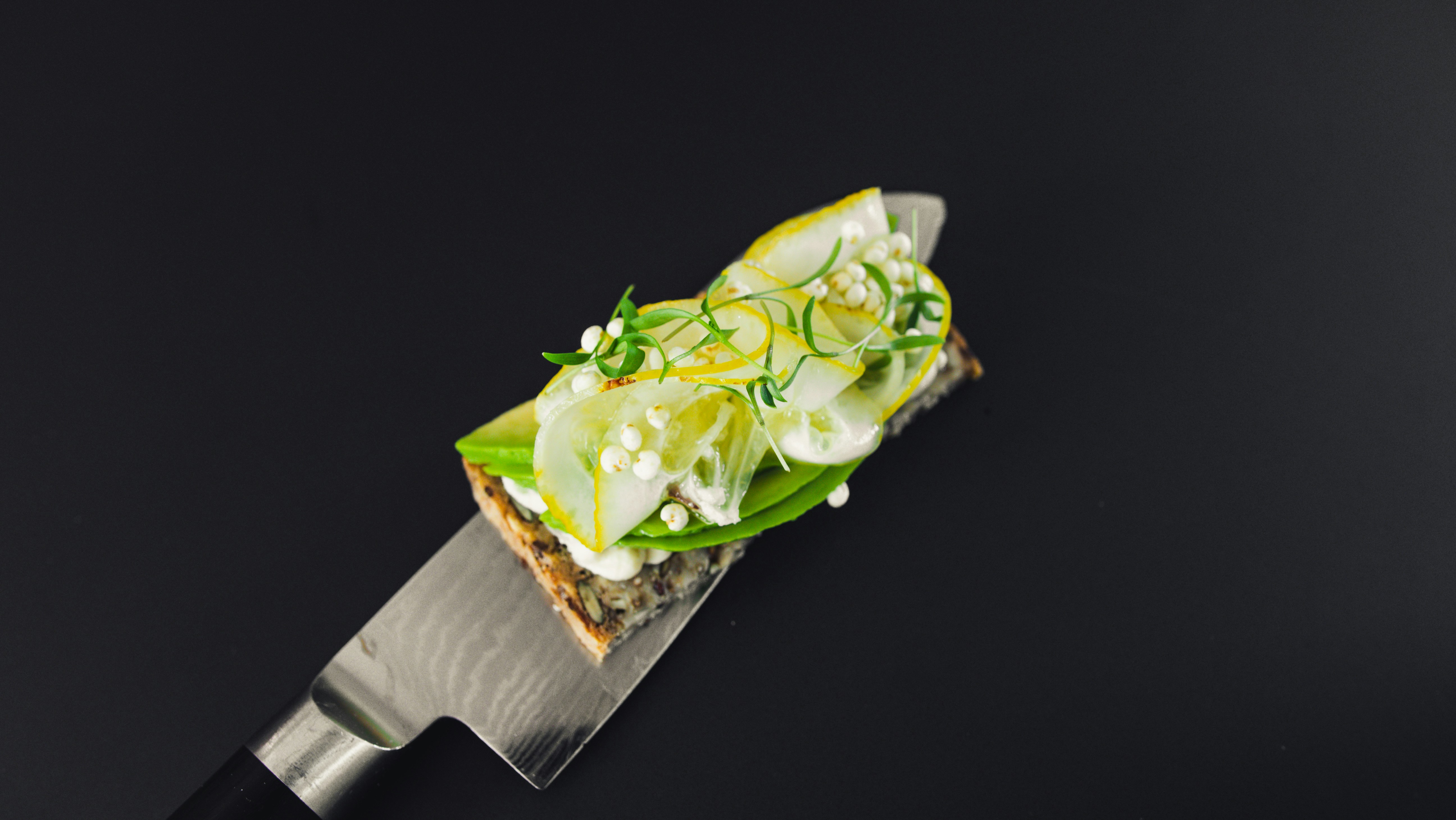 Cucumber toast on a knife against dark slate