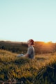 man in white shirt sitting on green grass field during sunset