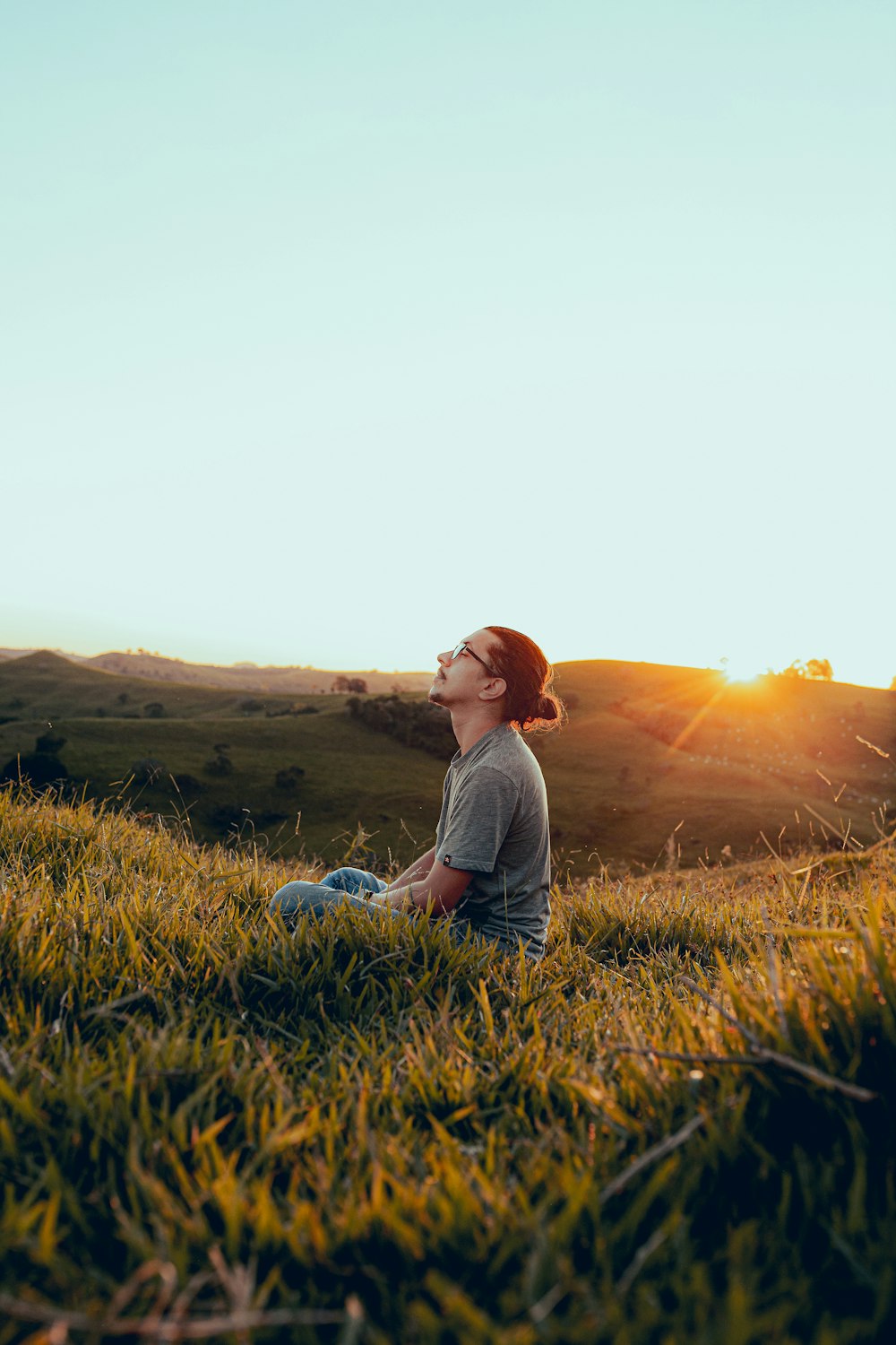 homme en chemise blanche assis sur le champ d’herbe verte pendant le coucher du soleil