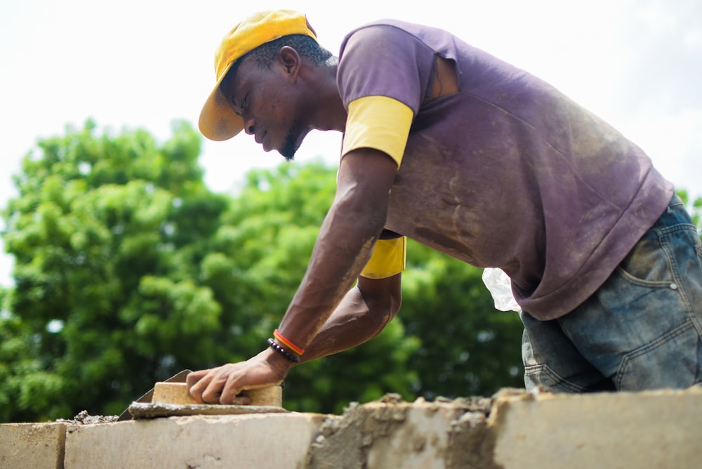 man in yellow t-shirt and blue denim jeans climbing on brown concrete wall during daytime