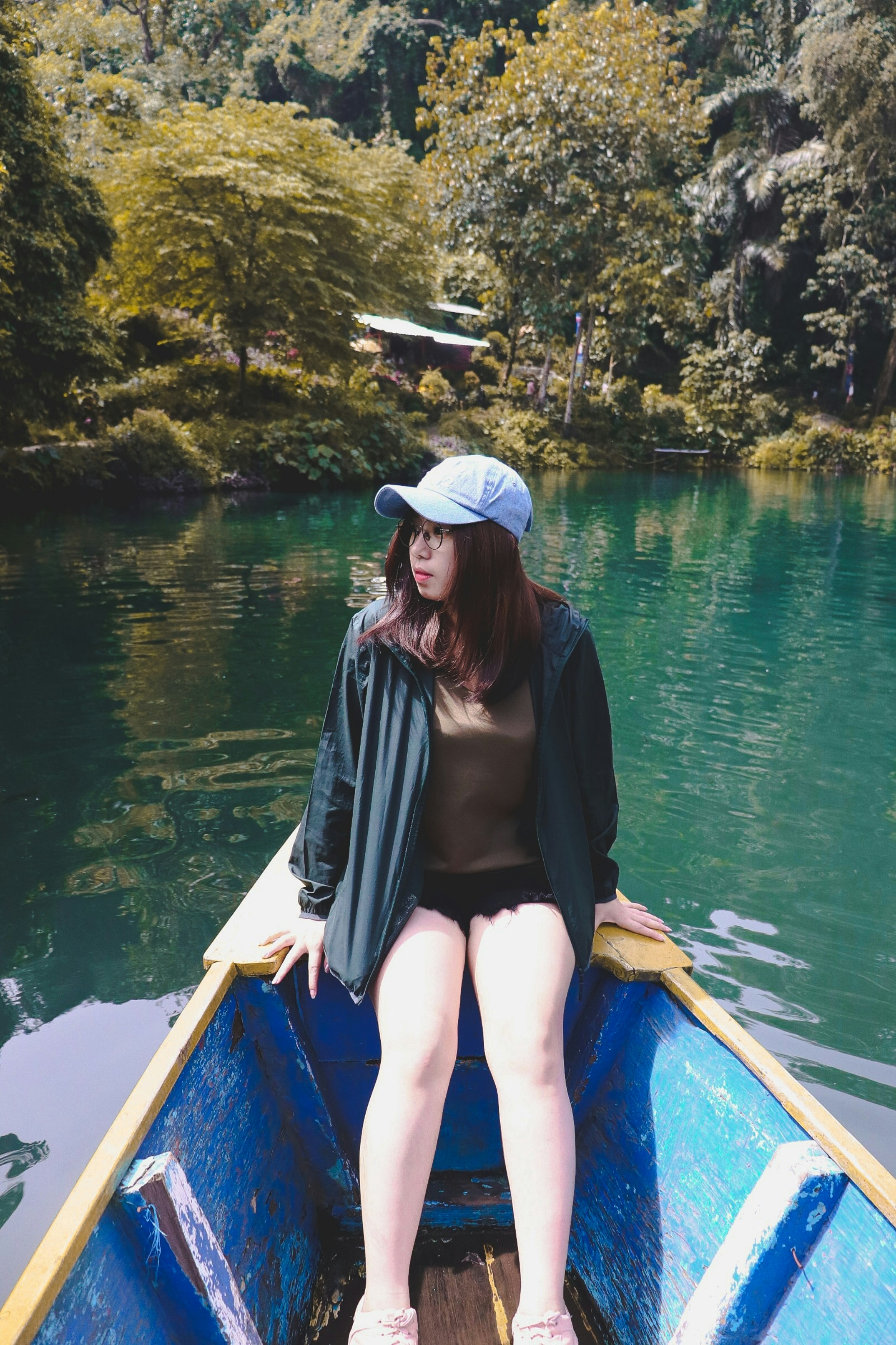 Wanita dengan tank top hitam dan topi putih duduk di perahu biru di siang hari