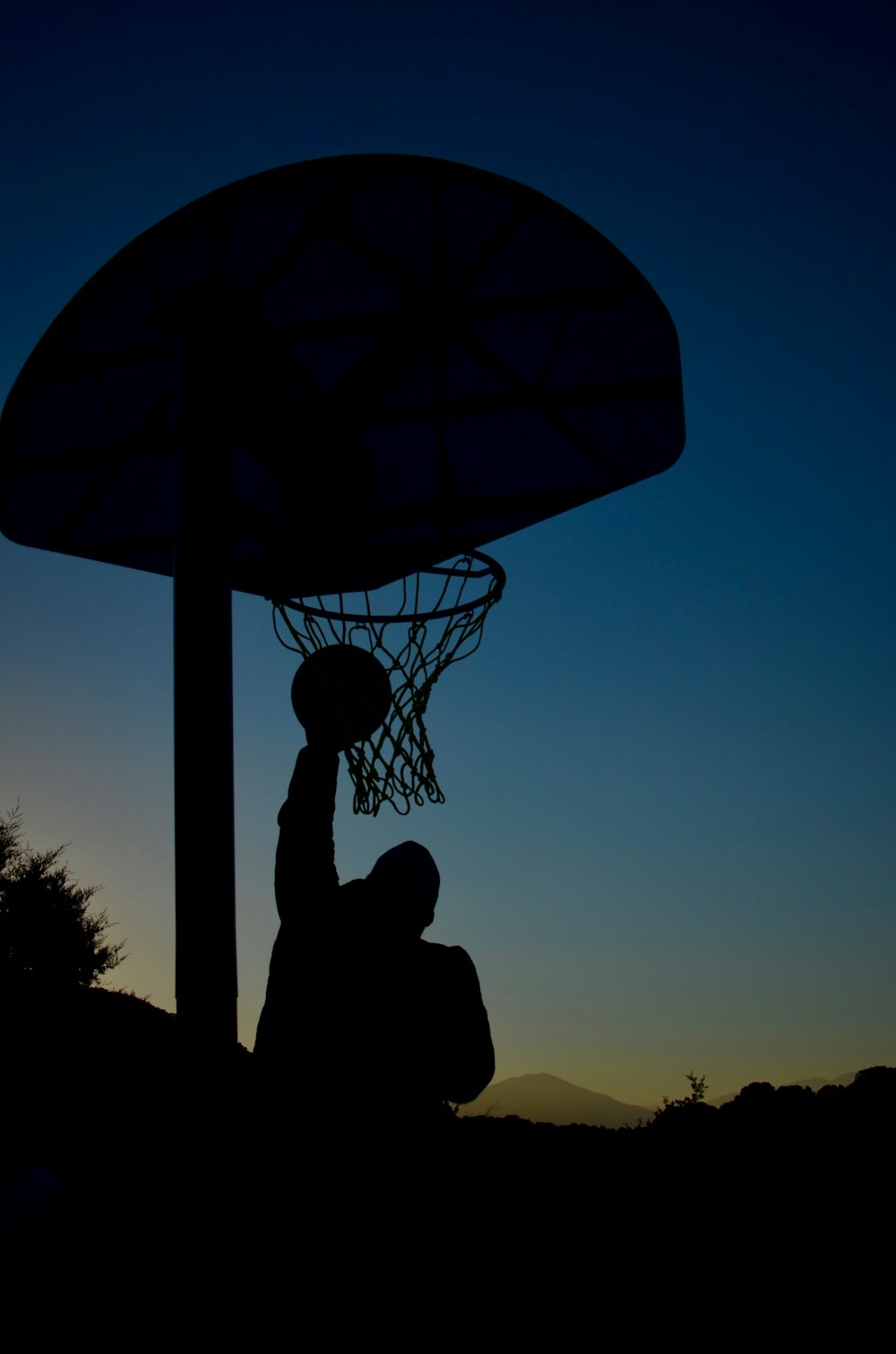 silhouette of person sitting under basketball hoop during daytime