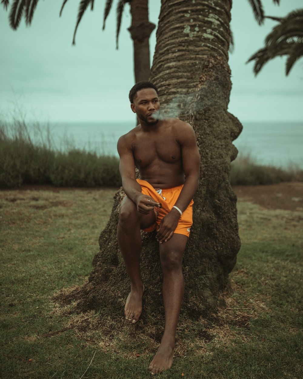 topless man in orange shorts leaning on brown rock