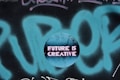 A circular graphic overlays a graffiti background with the phrase 'FUTURE IS CREATIVE' displayed in bold, neon pink letters on a cracked, textured blue surface.