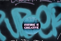 A circular graphic overlays a graffiti background with the phrase 'FUTURE IS CREATIVE' displayed in bold, neon pink letters on a cracked, textured blue surface.