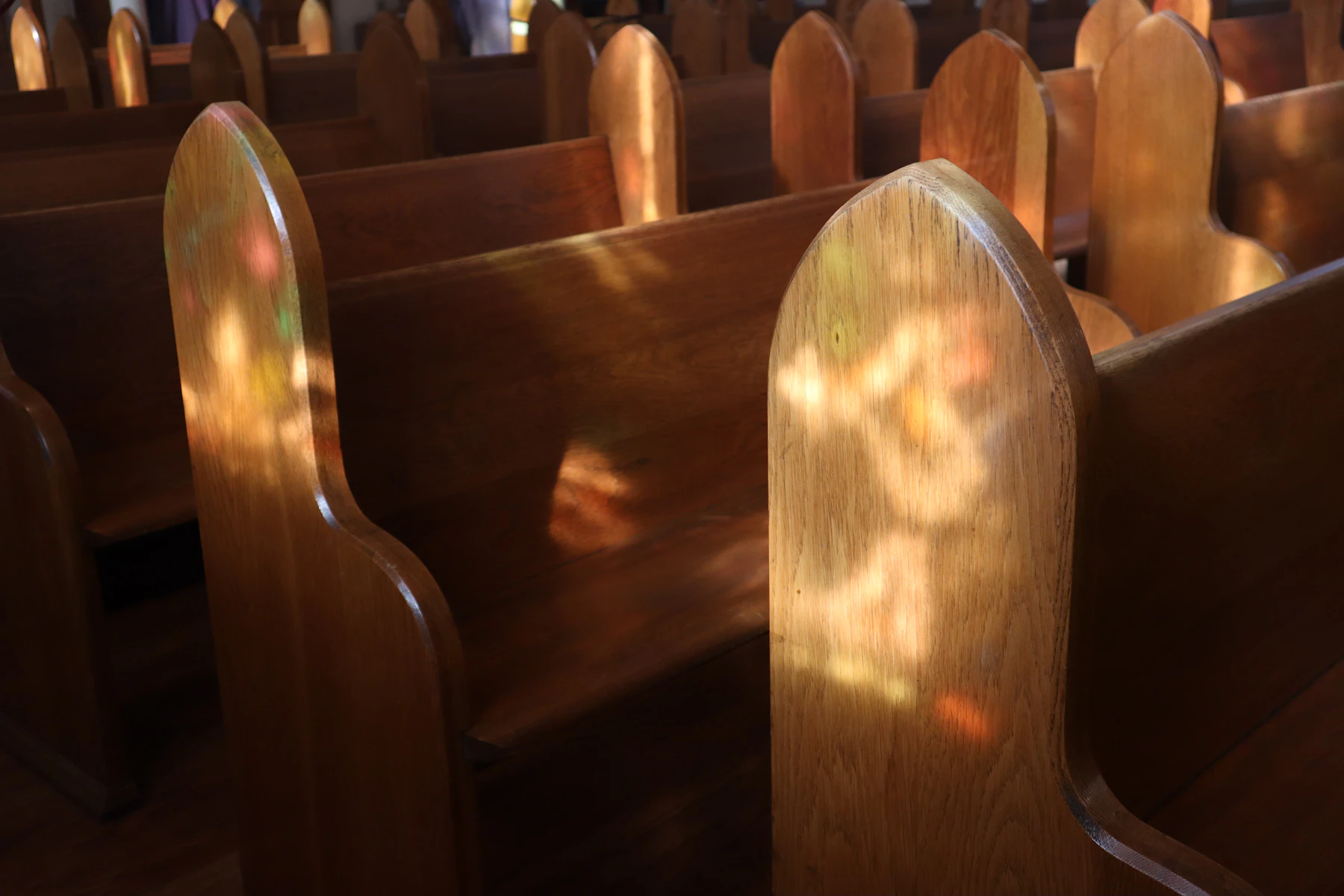 Wooden pews with patches of coloured light from a stained-glass window falling across them