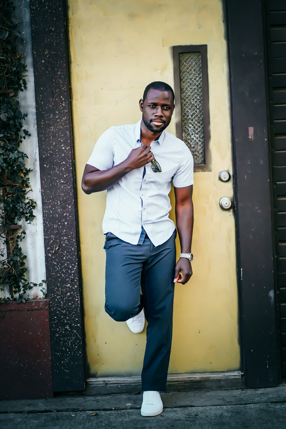 man in white button up t-shirt and blue denim jeans sitting on yellow door