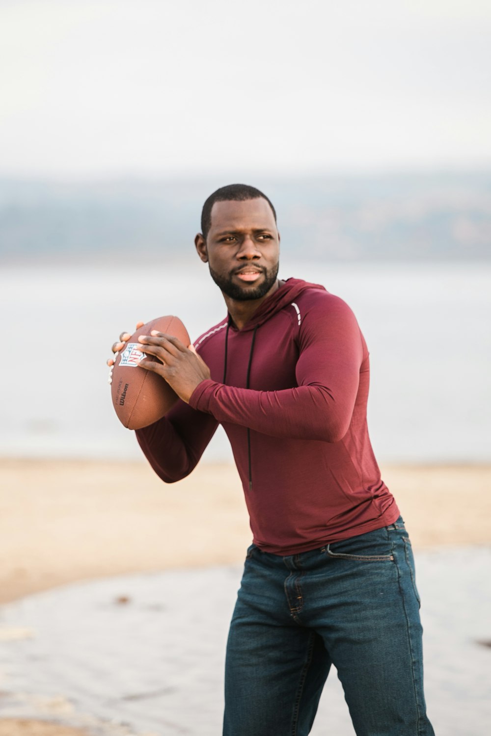 man in red long sleeve shirt and blue denim jeans holding brown cup