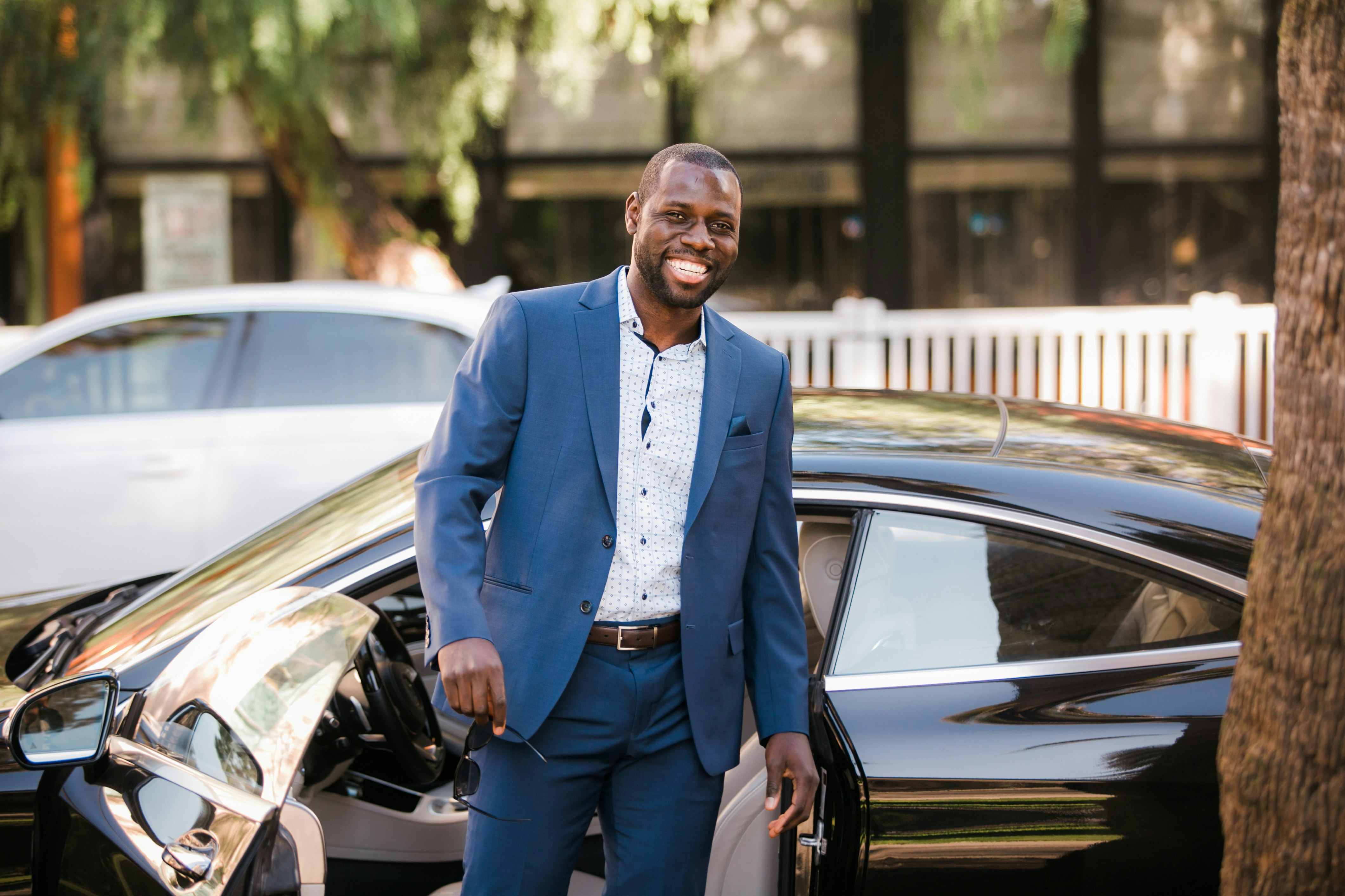Fortune Vieyra wearing a blue business suit and smiling in front of a Mercedes