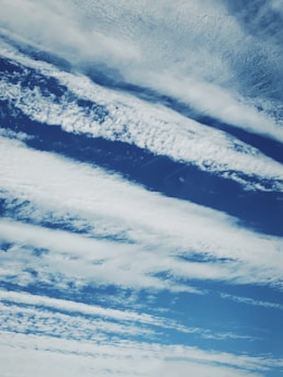 Cloud formations stretch across a rich blue sky, with varying textures and patterns creating a dynamic and serene scene.