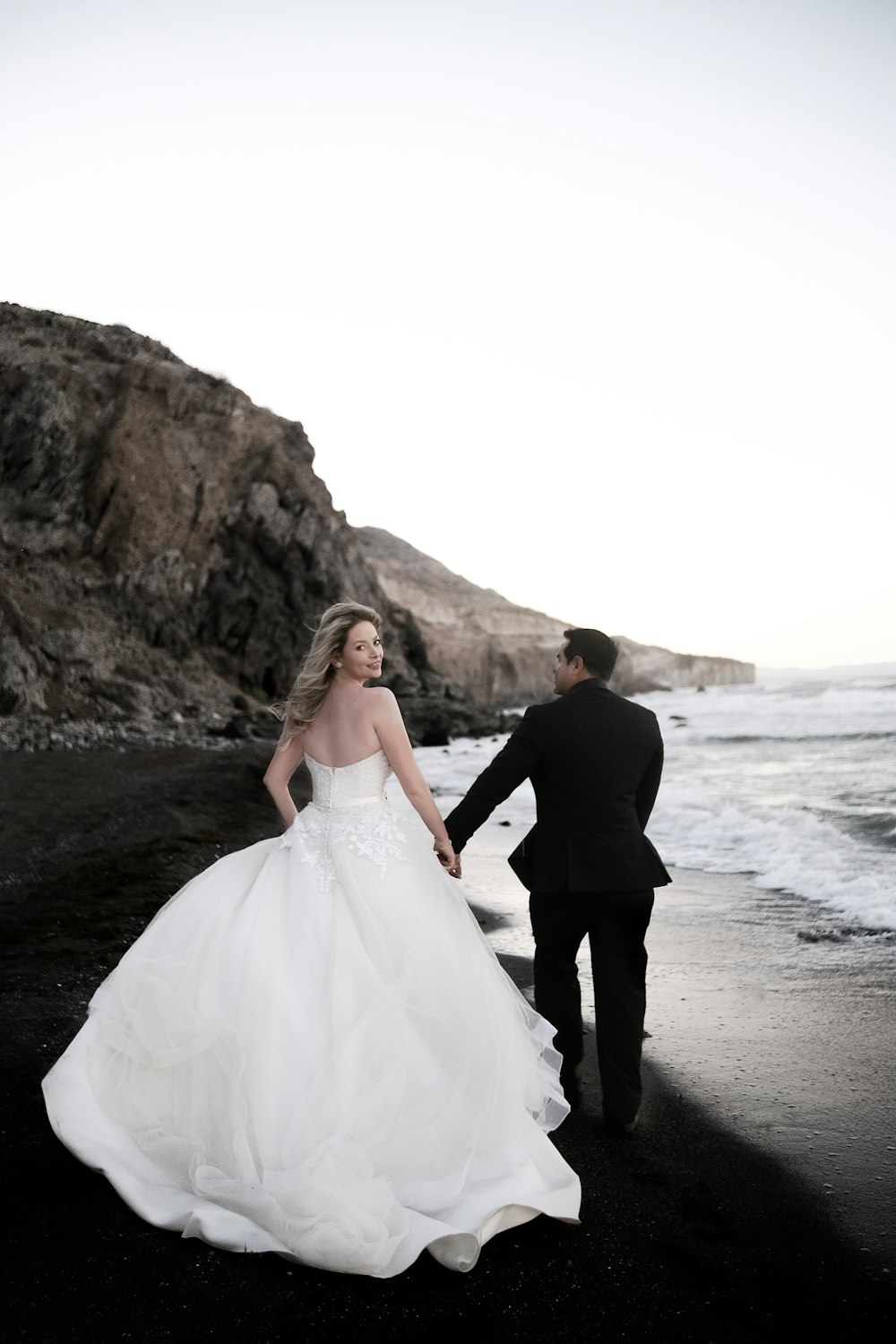 a bride and groom walking on the beach