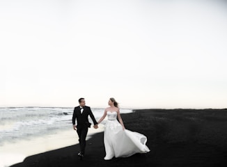 Bride and groom walking hand in hand along a quiet beach at sunset.