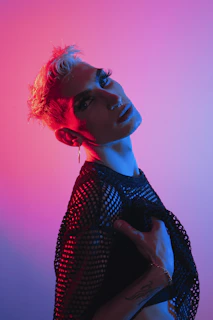 A bold queer model posing in a theatrical costume under high contrast lighting, embodying self-expression.
