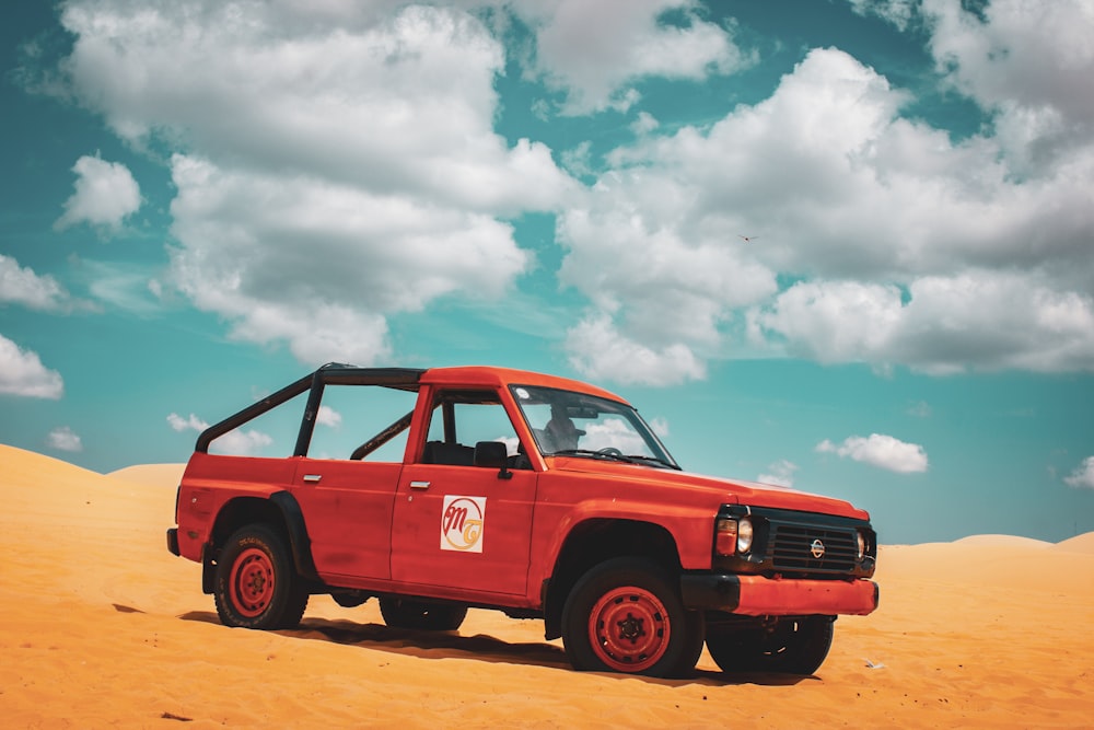 red suv on brown sand under white clouds and blue sky during daytime