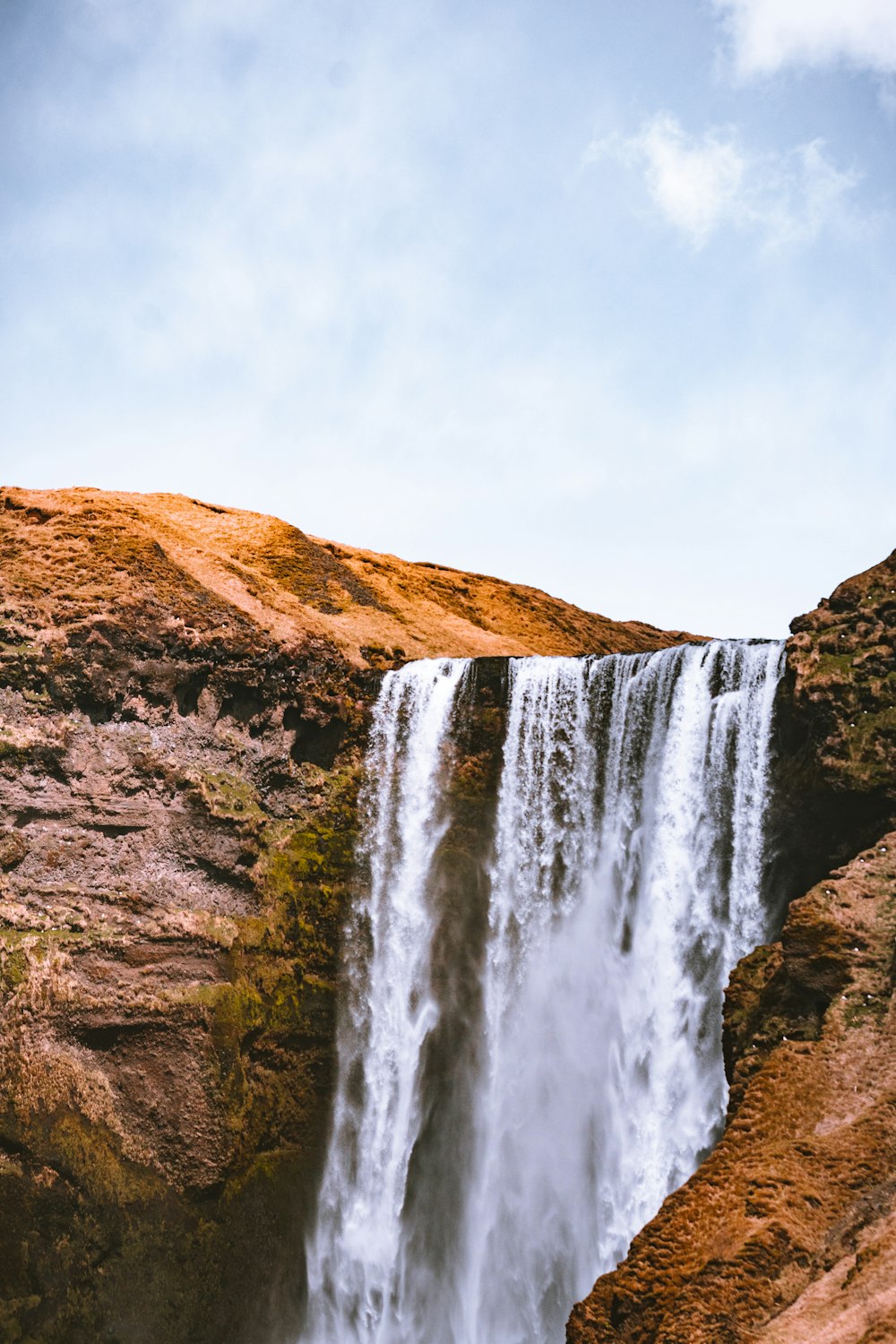 waterfalls on brown rocky mountain under white cloudy sky during daytime