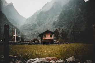 A spacious farmhouse with wooden accents set against the backdrop of misty Himalayan mountains.