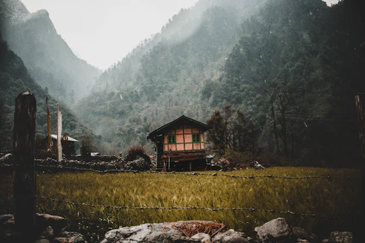 A spacious farmhouse with wooden accents set against the backdrop of misty Himalayan mountains.