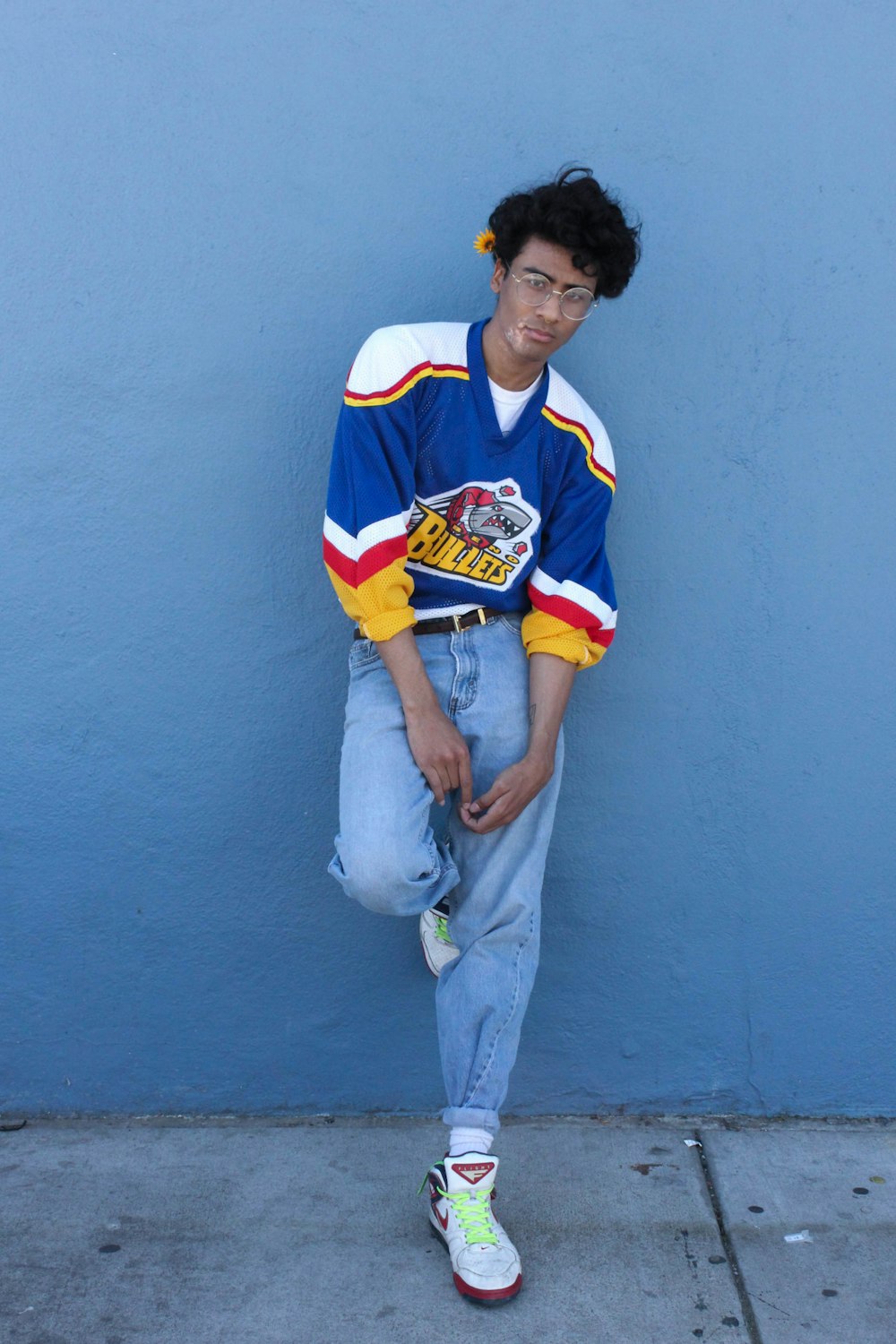 man in blue and white jersey shirt and gray pants leaning on blue wall