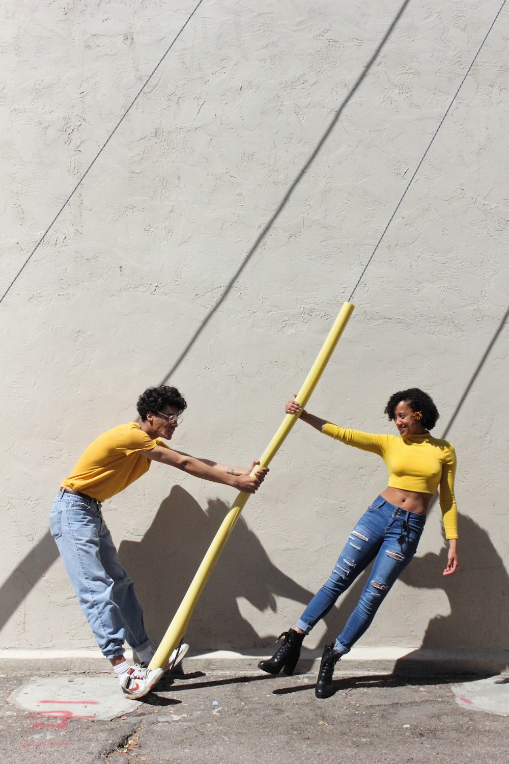 man in yellow shirt and blue denim jeans holding brown wooden stick