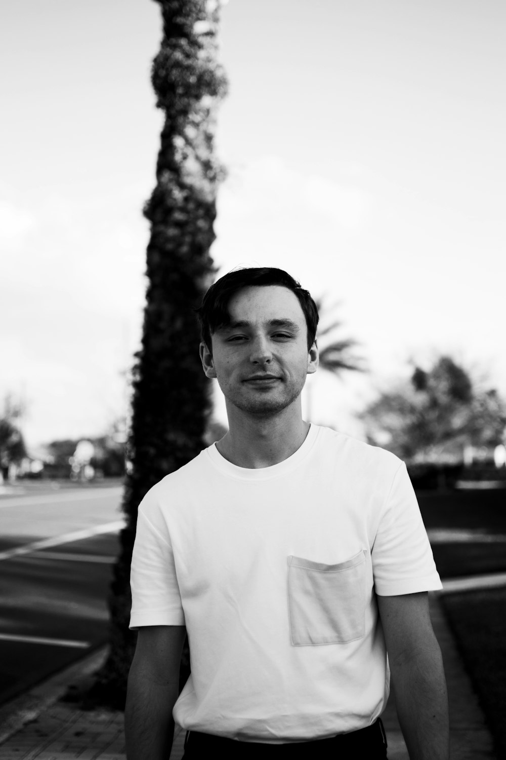 man in crew neck t-shirt standing on road in grayscale photography