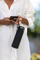 Hands holding a water bottle and a smartphone showing a fitness app.